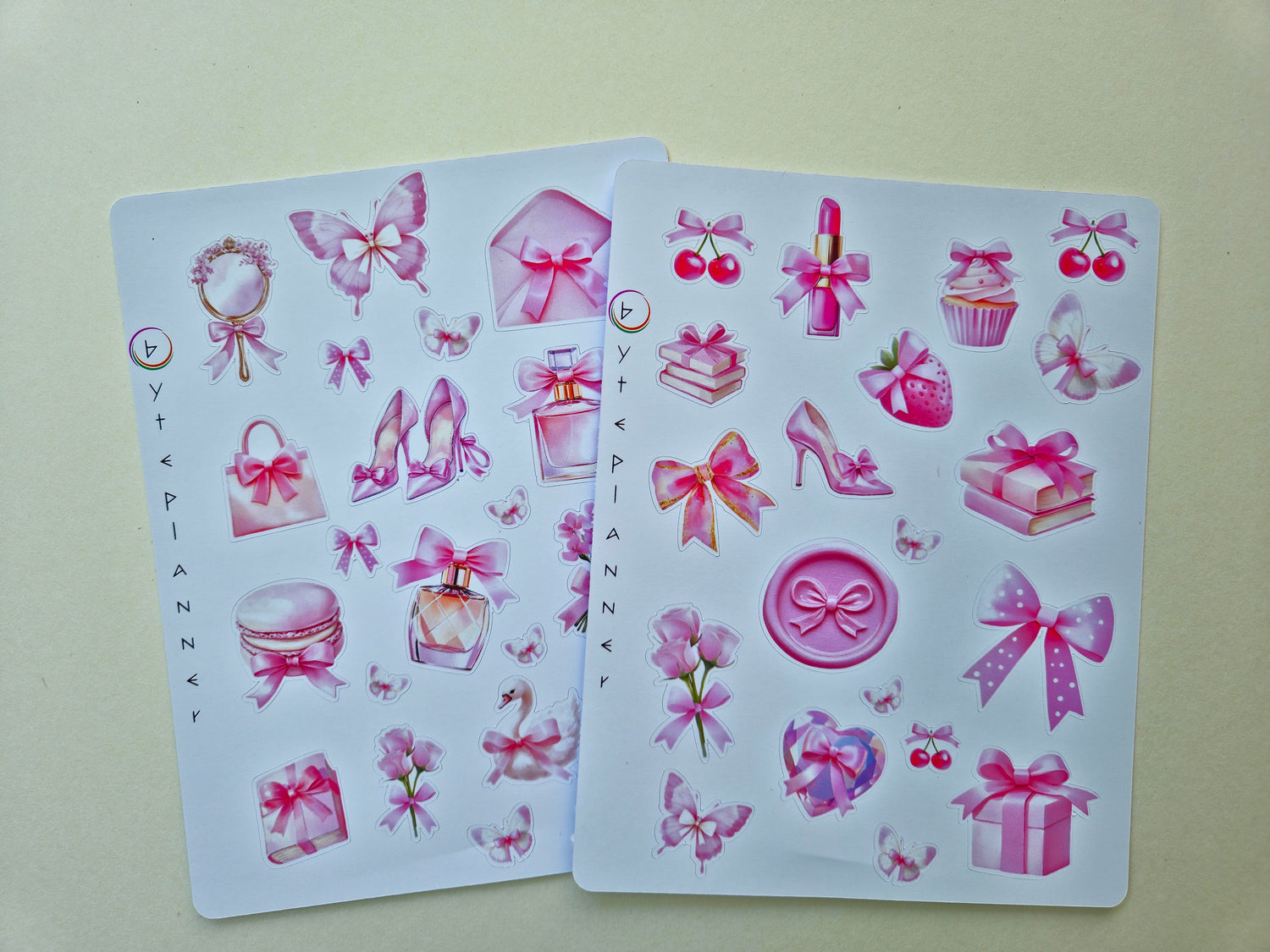 Zwei Stickerbögen im Format 13 × 17 cm mit romantischen pastellrosa Motiven (Schleifen, Parfumflakon, Geschenkboxen, Cupcake, Erdbeere, Kirschen, Blumen und Schmetterlinge) auf weißem Hintergrund