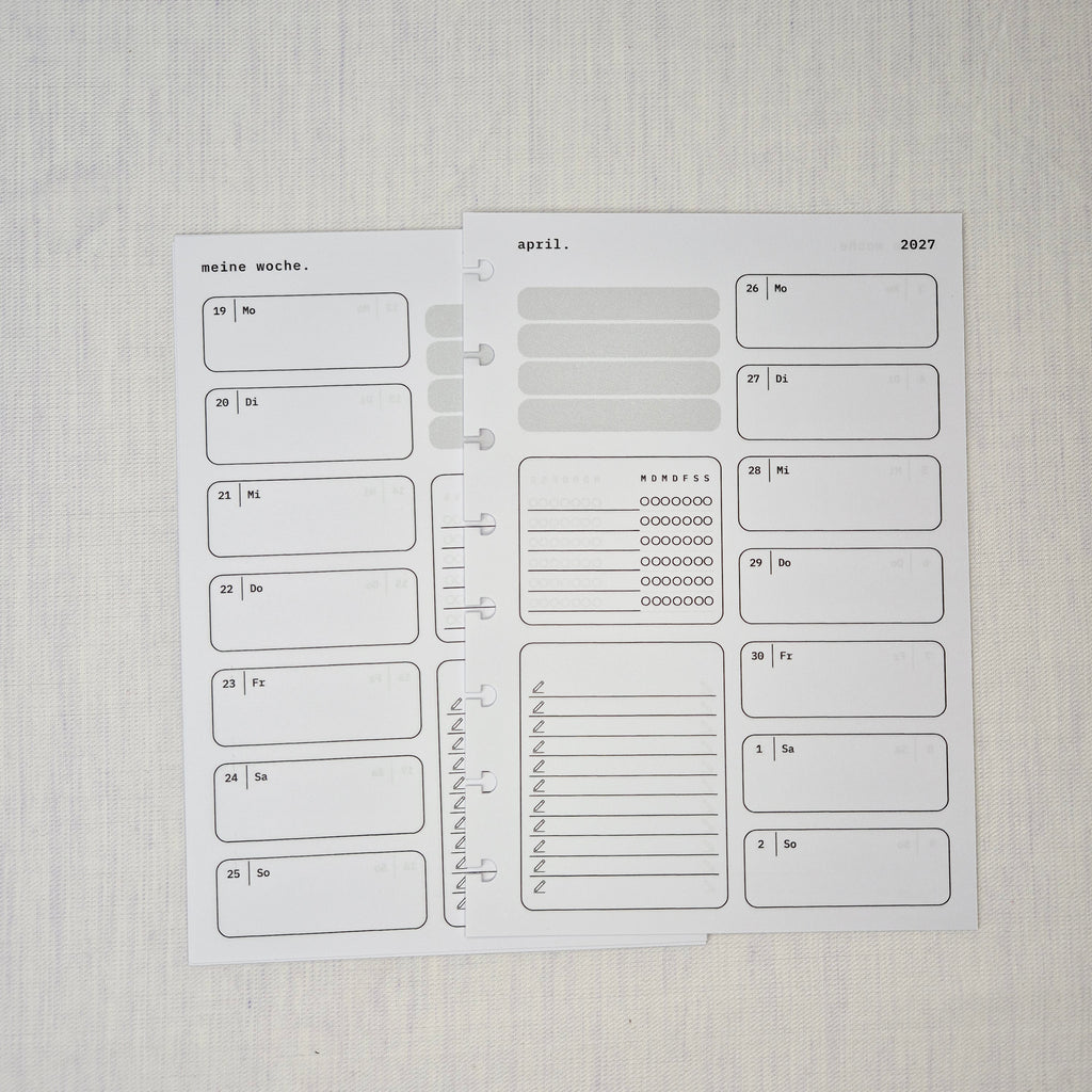 Zwei nebeneinanderliegende Planer-Einlagenseiten im minimalistischen Grau-Beige-Design mit der Überschrift WOCHE AUF 1 SEITE. Links eine Wochenübersicht ‘meine woche.’ mit Boxen für Mo–So und kleinen Datumsfeldern; rechts die Fortsetzung derselben Woche mit Boxen für Mo–So und dem Monatskopf ‘januar’ sowie Jahreszahl ‘2027’. In beiden Seiten gibt es zusätzlich neutrale Platzhalterfelder, einen kleinen Habit-Tracker mit Kreisen und einen linierten Notiz-/To-do-Bereich. Am Rand sind Lochungen/Discs-Markierung