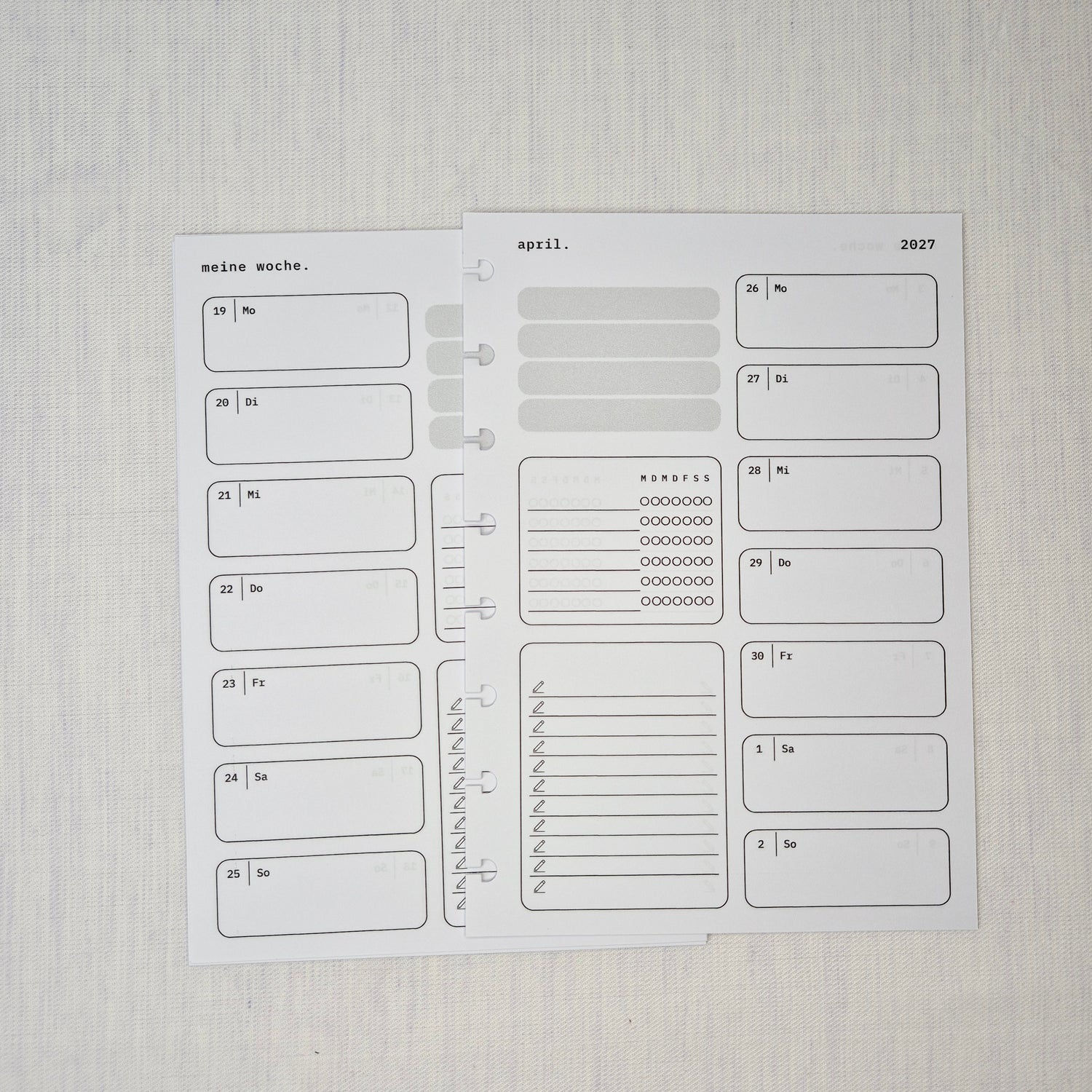 Zwei nebeneinanderliegende Planer-Einlagenseiten im minimalistischen Grau-Beige-Design mit der Überschrift WOCHE AUF 1 SEITE. Links eine Wochenübersicht ‘meine woche.’ mit Boxen für Mo–So und kleinen Datumsfeldern; rechts die Fortsetzung derselben Woche mit Boxen für Mo–So und dem Monatskopf ‘januar’ sowie Jahreszahl ‘2027’. In beiden Seiten gibt es zusätzlich neutrale Platzhalterfelder, einen kleinen Habit-Tracker mit Kreisen und einen linierten Notiz-/To-do-Bereich. Am Rand sind Lochungen/Discs-Markierung