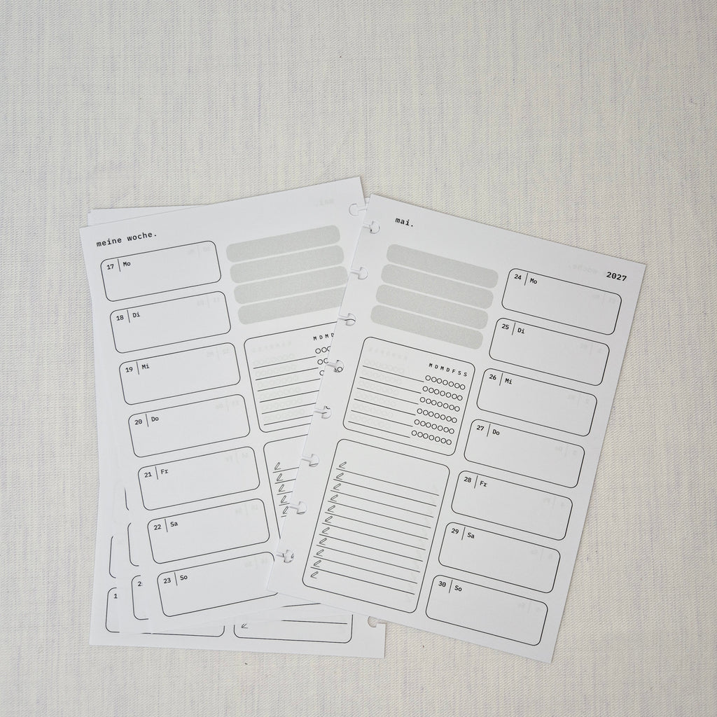 Zwei nebeneinanderliegende Planer-Einlagenseiten im minimalistischen Grau-Beige-Design mit der Überschrift WOCHE AUF 1 SEITE. Links eine Wochenübersicht ‘meine woche.’ mit Boxen für Mo–So und kleinen Datumsfeldern; rechts die Fortsetzung derselben Woche mit Boxen für Mo–So und dem Monatskopf ‘januar’ sowie Jahreszahl ‘2027’. In beiden Seiten gibt es zusätzlich neutrale Platzhalterfelder, einen kleinen Habit-Tracker mit Kreisen und einen linierten Notiz-/To-do-Bereich. Am Rand sind Lochungen/Discs-Markierung