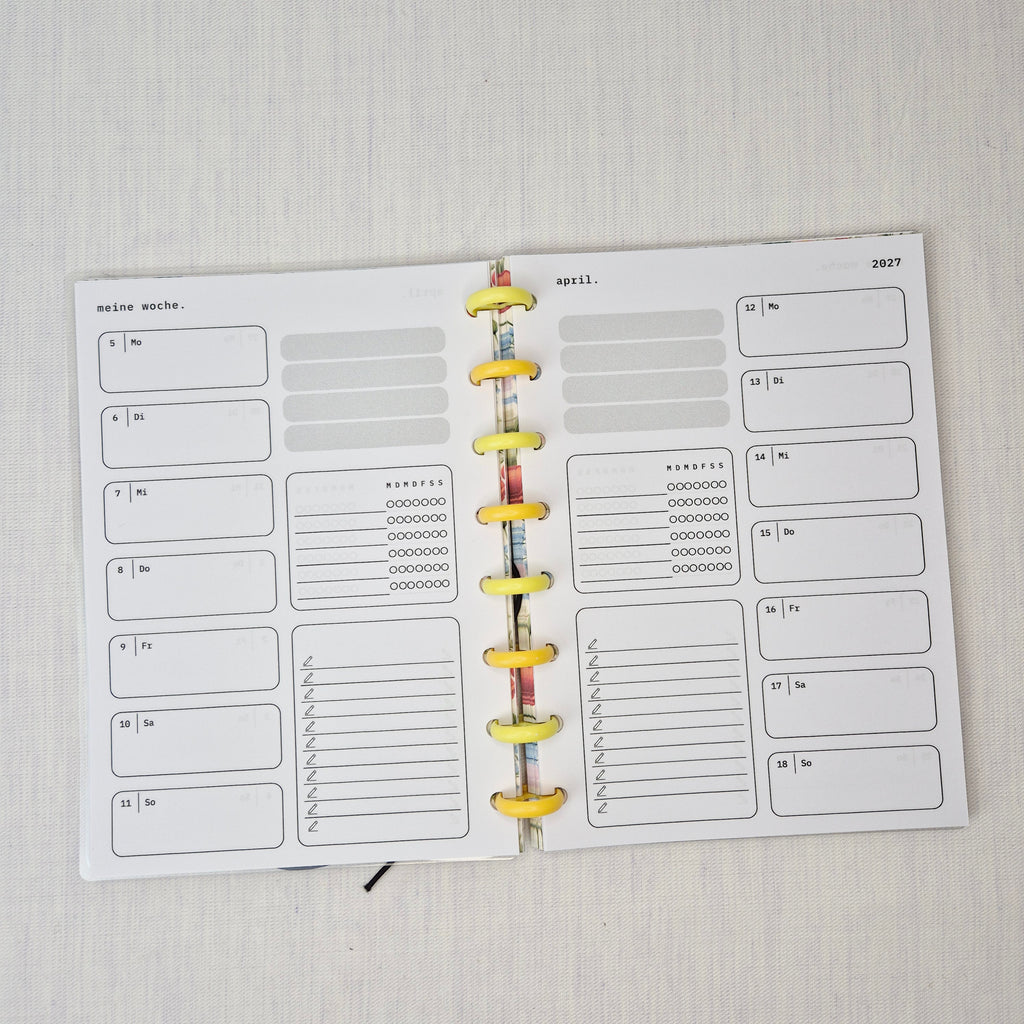 Zwei nebeneinanderliegende Planer-Einlagenseiten im minimalistischen Grau-Beige-Design mit der Überschrift WOCHE AUF 1 SEITE. Links eine Wochenübersicht ‘meine woche.’ mit Boxen für Mo–So und kleinen Datumsfeldern; rechts die Fortsetzung derselben Woche mit Boxen für Mo–So und dem Monatskopf ‘januar’ sowie Jahreszahl ‘2027’. In beiden Seiten gibt es zusätzlich neutrale Platzhalterfelder, einen kleinen Habit-Tracker mit Kreisen und einen linierten Notiz-/To-do-Bereich. Am Rand sind Lochungen/Discs-Markierung