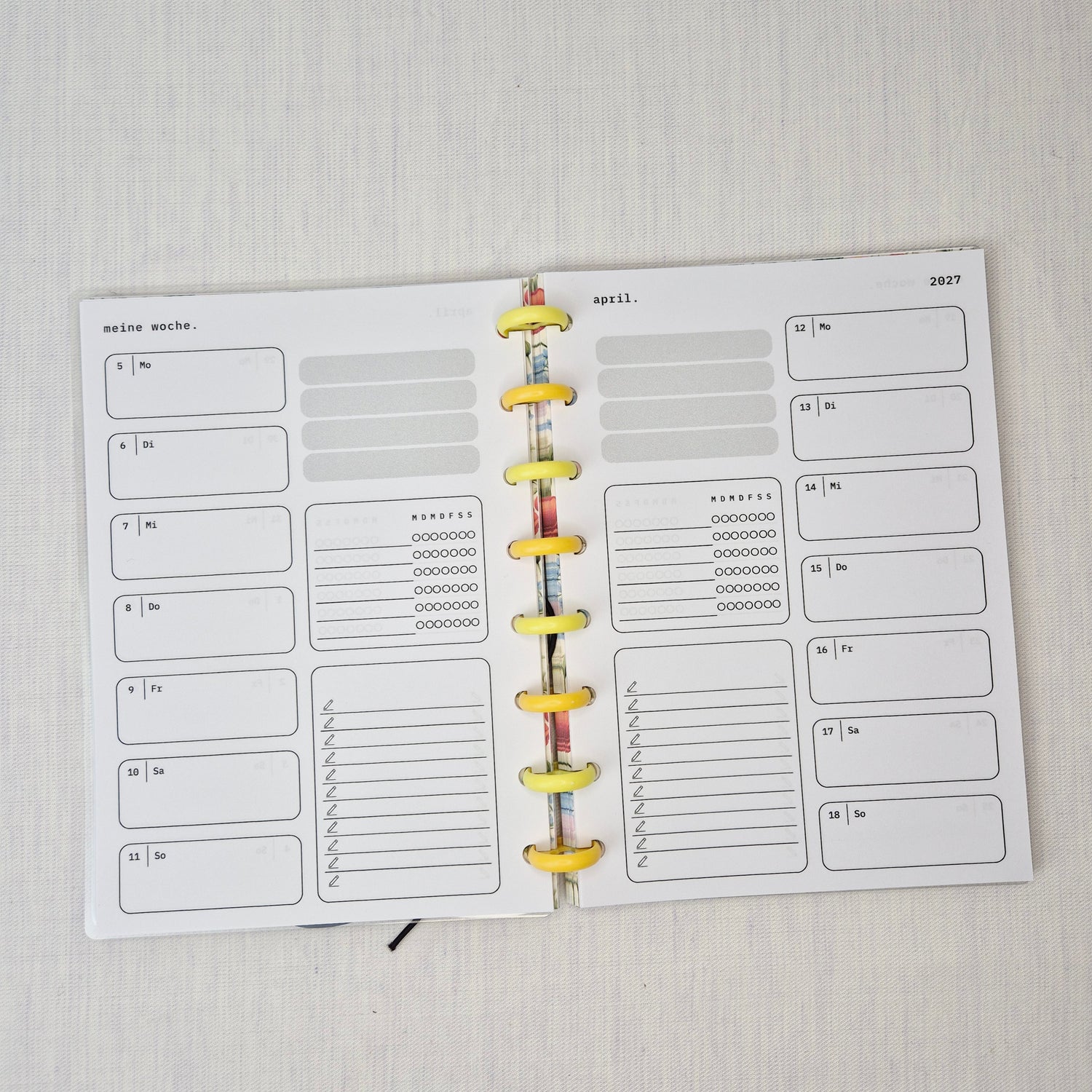 Zwei nebeneinanderliegende Planer-Einlagenseiten im minimalistischen Grau-Beige-Design mit der Überschrift WOCHE AUF 1 SEITE. Links eine Wochenübersicht ‘meine woche.’ mit Boxen für Mo–So und kleinen Datumsfeldern; rechts die Fortsetzung derselben Woche mit Boxen für Mo–So und dem Monatskopf ‘januar’ sowie Jahreszahl ‘2027’. In beiden Seiten gibt es zusätzlich neutrale Platzhalterfelder, einen kleinen Habit-Tracker mit Kreisen und einen linierten Notiz-/To-do-Bereich. Am Rand sind Lochungen/Discs-Markierung