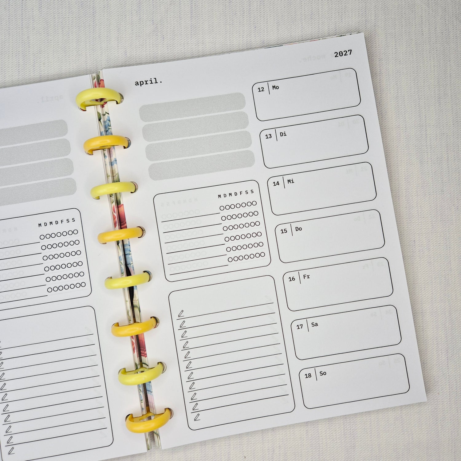 Zwei nebeneinanderliegende Planer-Einlagenseiten im minimalistischen Grau-Beige-Design mit der Überschrift WOCHE AUF 1 SEITE. Links eine Wochenübersicht ‘meine woche.’ mit Boxen für Mo–So und kleinen Datumsfeldern; rechts die Fortsetzung derselben Woche mit Boxen für Mo–So und dem Monatskopf ‘januar’ sowie Jahreszahl ‘2027’. In beiden Seiten gibt es zusätzlich neutrale Platzhalterfelder, einen kleinen Habit-Tracker mit Kreisen und einen linierten Notiz-/To-do-Bereich. Am Rand sind Lochungen/Discs-Markierung