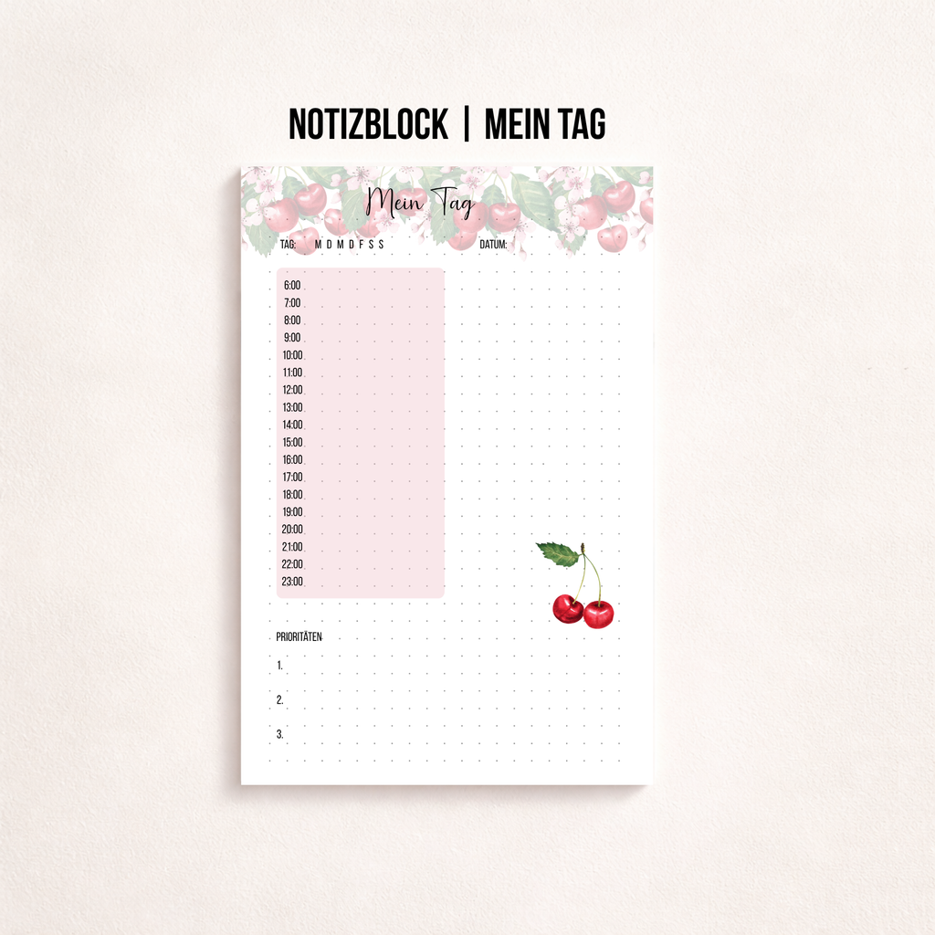 Gedruckter A6-Tagesplanerblock „Mein Tag“ mit zarter rosa Kirschbordüre, Feldern für Wochentag und Datum, Stundenplan von 6 bis 23 Uhr, Dot-Grid-Notizfeld und Prioritätenliste. Unten rechts ist eine kleine Kirschen-Illustration zu sehen.