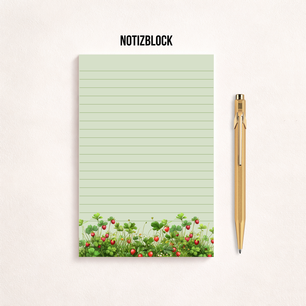 Liniertes Notizpapier im Hochformat mit grün-rosa Erdbeerwiesen-Motiv am unteren Rand, fotografiert auf dunkelgrauem Hintergrund. Links daneben liegt ein transparenter Stift parallel zum Block. Cleanes, minimalistisches Flatlay mit viel freiem Raum