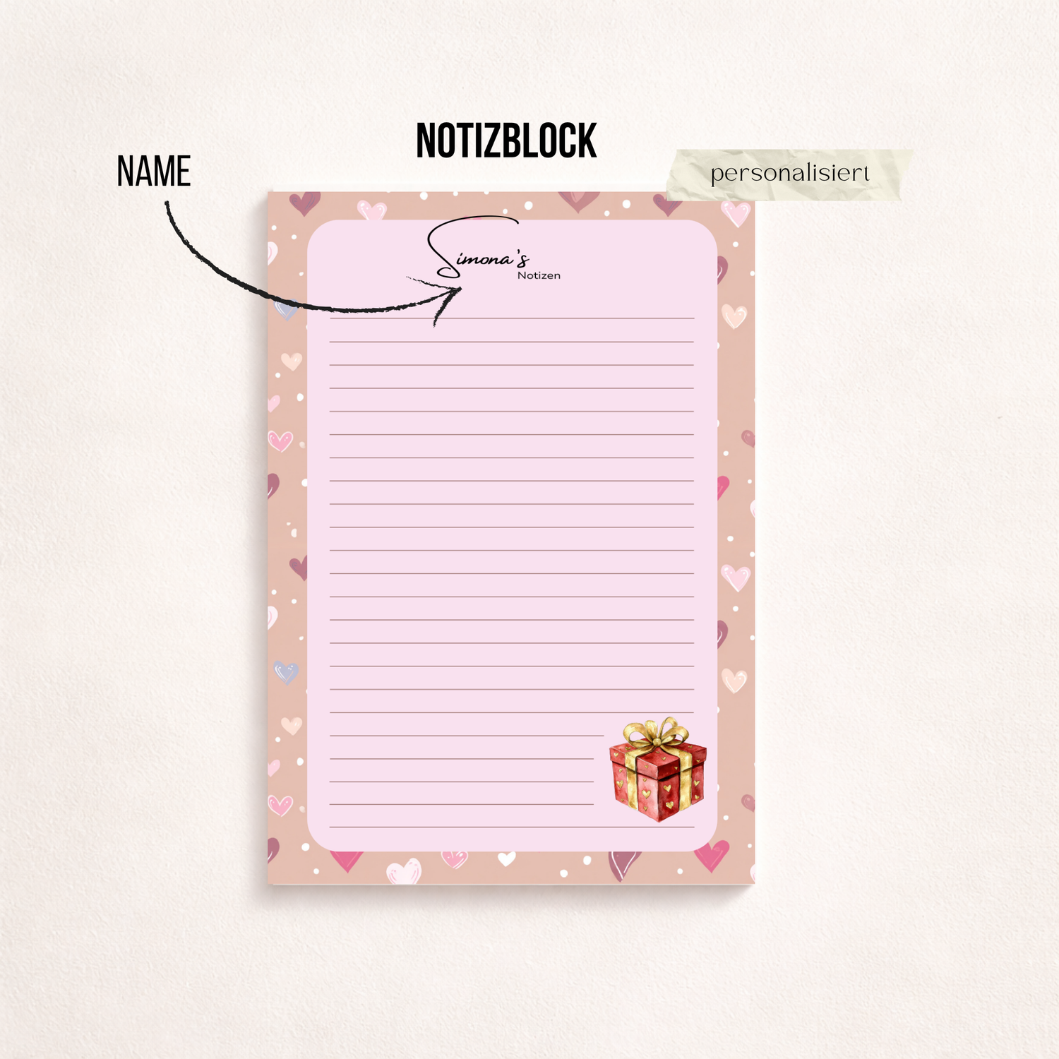 A5-Notizblock mit rosa Herzrand und gepunkteter Schreibfläche auf dunklem Hintergrund. Unten rechts ist ein kleines Geschenkmotiv abgebildet.