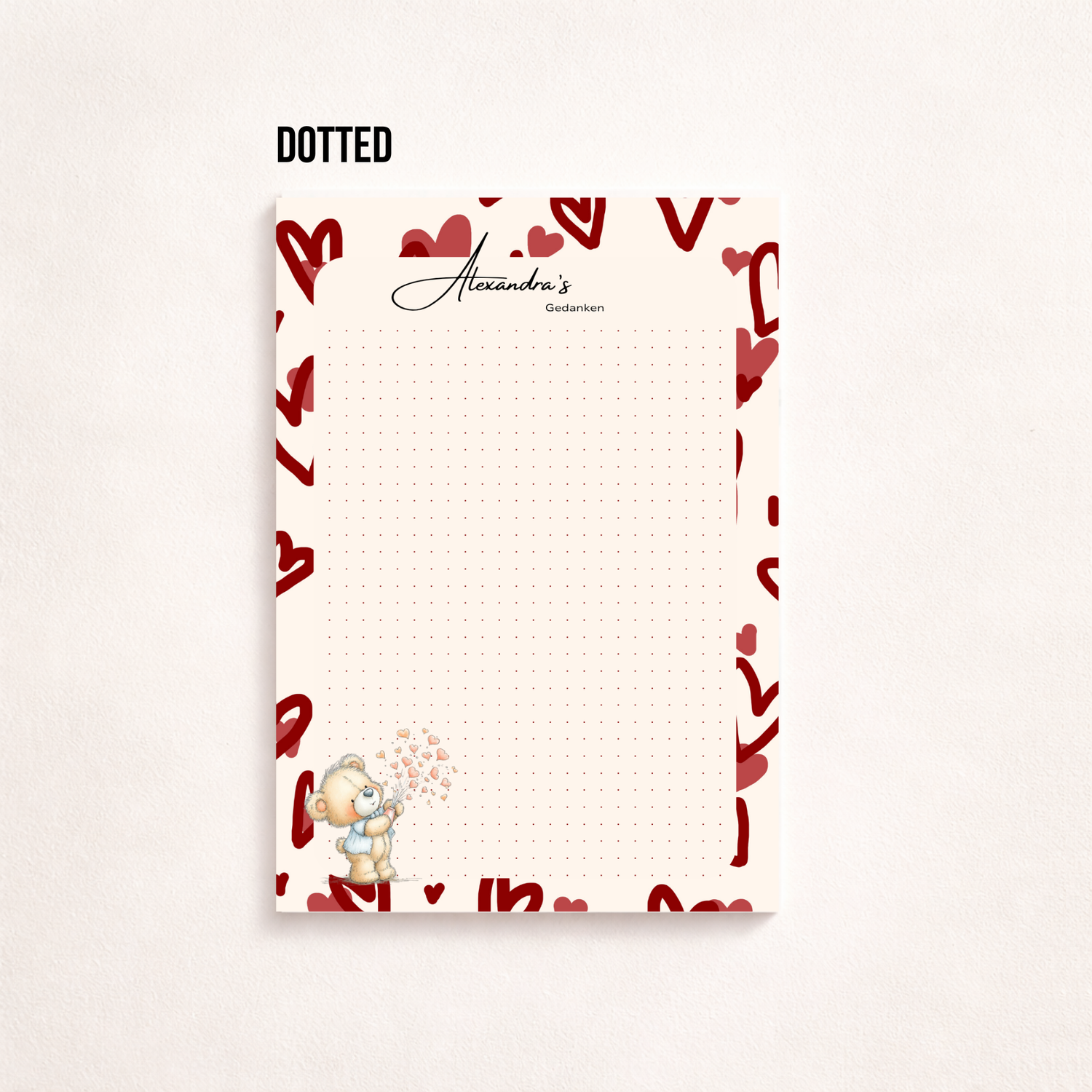 A5-Notizblatt mit rosa Herzmuster am Rand, personalisiert mit „Alexandra’s Gedanken“, linierten Schreibzeilen und kleinem Teddybär mit Herzen unten links