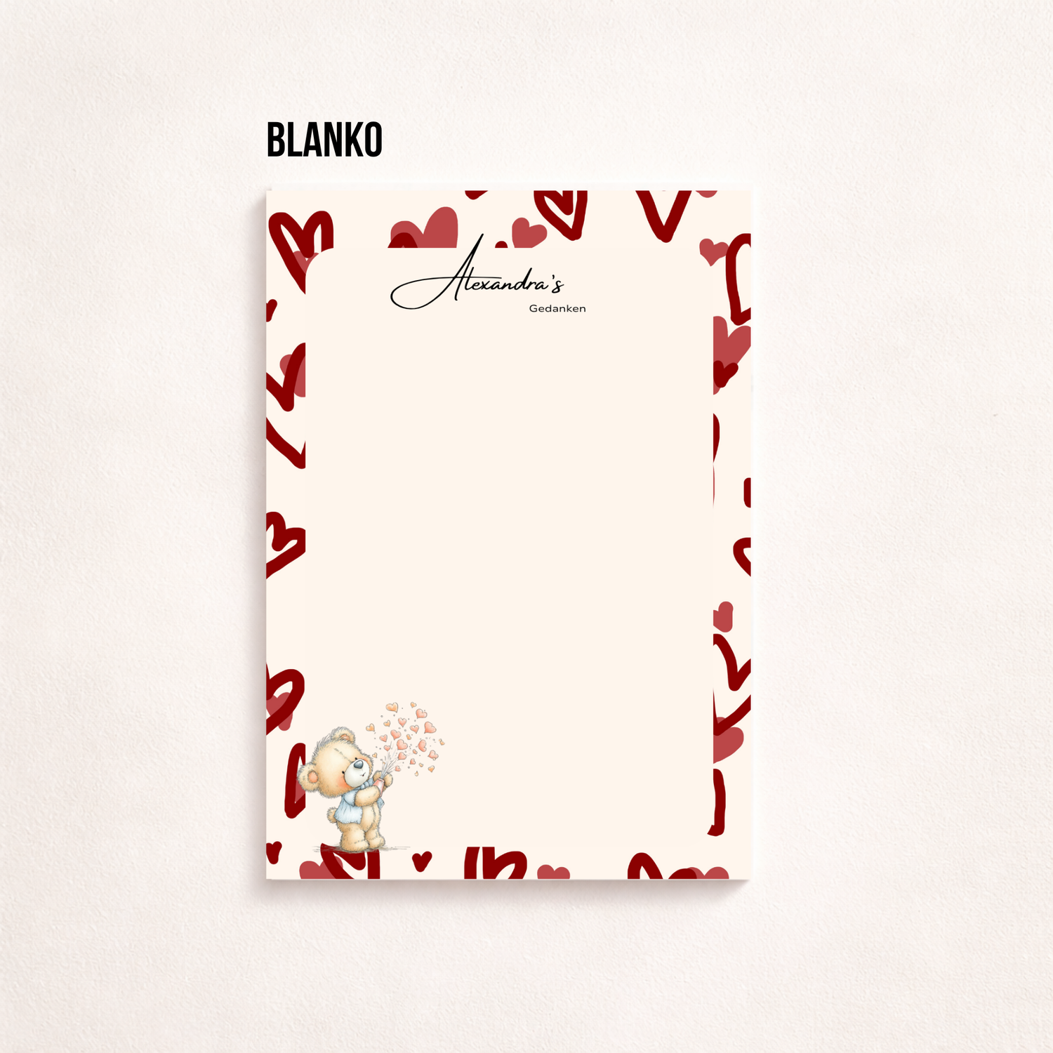 A5-Notizblatt mit rosa Herzmuster am Rand, personalisiert mit „Alexandra’s Gedanken“, linierten Schreibzeilen und kleinem Teddybär mit Herzen unten links