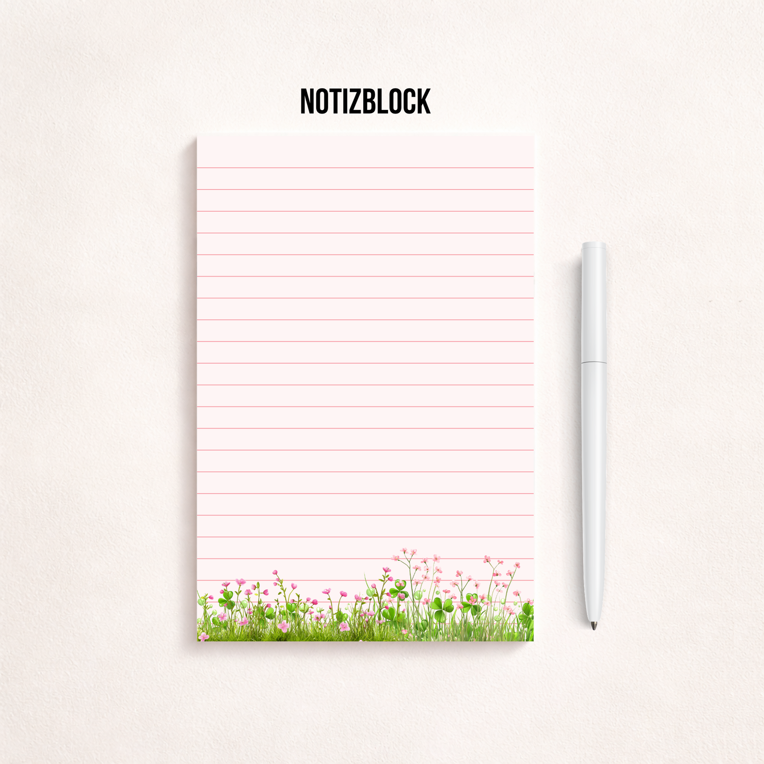 Minimalistischer, rosa linierter Notizblock mit Blumenwiesen-Motiv am unteren Rand auf hellem Hintergrund, rechts daneben ein goldener Kugelschreiber, darüber der Schriftzug „NOTIZBLOCK“
