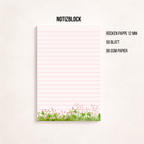 Minimalistischer, rosa linierter Notizblock mit Blumenwiesen-Motiv am unteren Rand auf hellem Hintergrund, rechts daneben ein goldener Kugelschreiber, darüber der Schriftzug „NOTIZBLOCK“