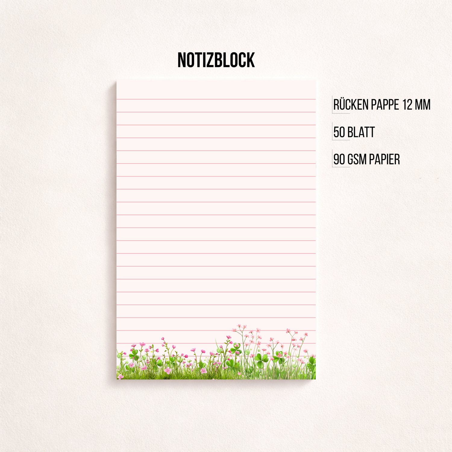 Minimalistischer, rosa linierter Notizblock mit Blumenwiesen-Motiv am unteren Rand auf hellem Hintergrund, rechts daneben ein goldener Kugelschreiber, darüber der Schriftzug „NOTIZBLOCK“
