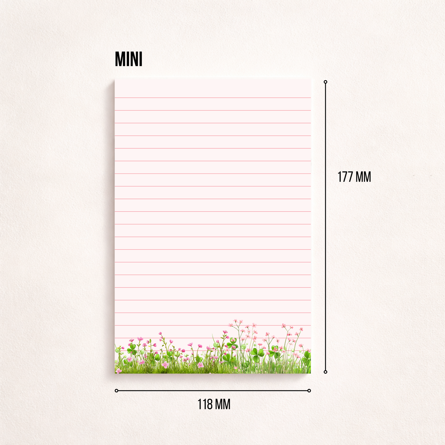 Minimalistischer, rosa linierter Notizblock mit Blumenwiesen-Motiv am unteren Rand auf hellem Hintergrund, rechts daneben ein goldener Kugelschreiber, darüber der Schriftzug „NOTIZBLOCK“
