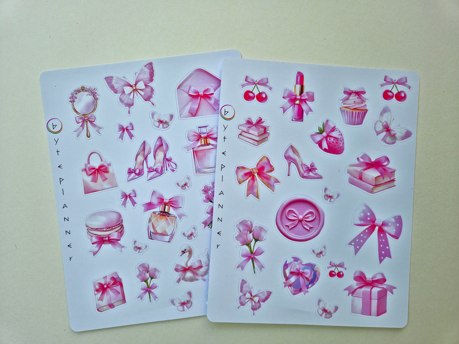 Zwei Stickerbögen im Format 13 × 17 cm mit romantischen pastellrosa Motiven (Schleifen, Parfumflakon, Geschenkboxen, Cupcake, Erdbeere, Kirschen, Blumen und Schmetterlinge) auf weißem Hintergrund